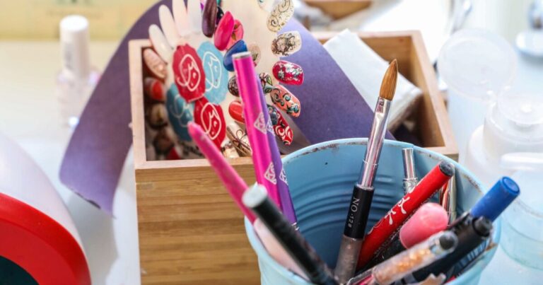 A nail technician workstation with art brushes in a pot, polish bottles and painted sample tips