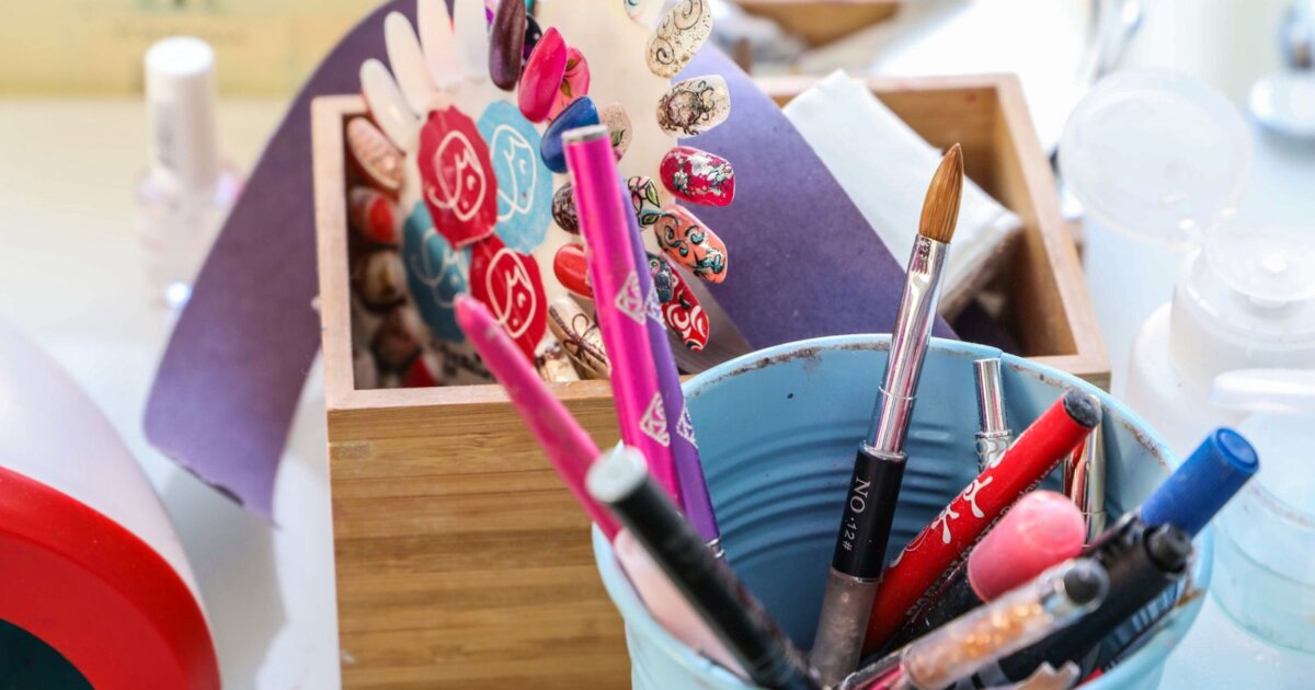 A nail technician workstation with art brushes in a pot, polish bottles and painted sample tips