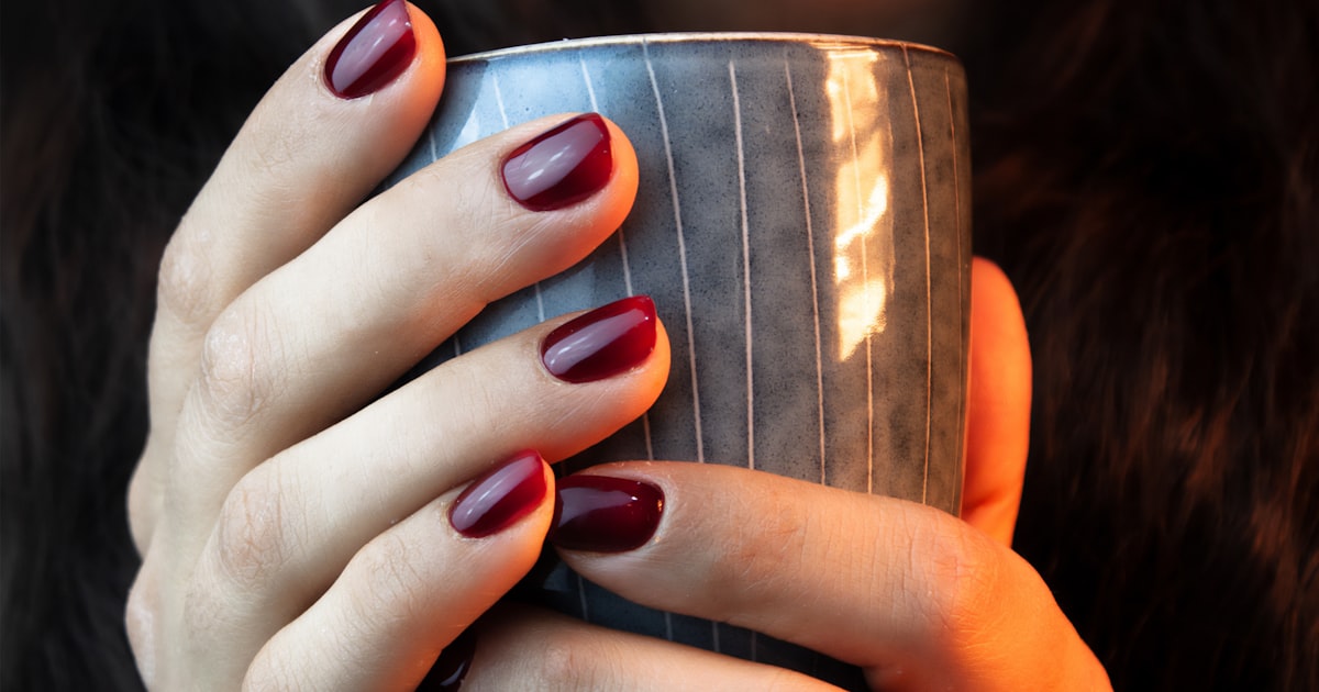 Warm terracotta orange nails wrapped around a coffee cup