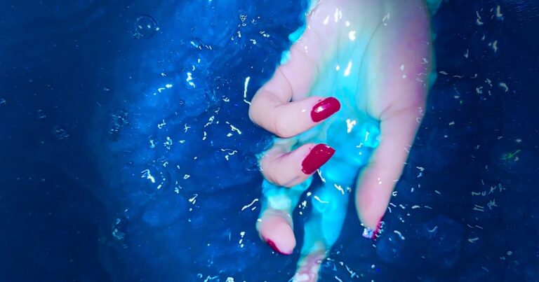 Red nails with a glossy finish, hand resting in water
