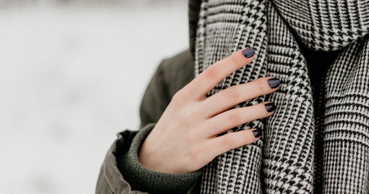 Dark winter manicure against a houndstooth scarf, the moody-luxe nail look