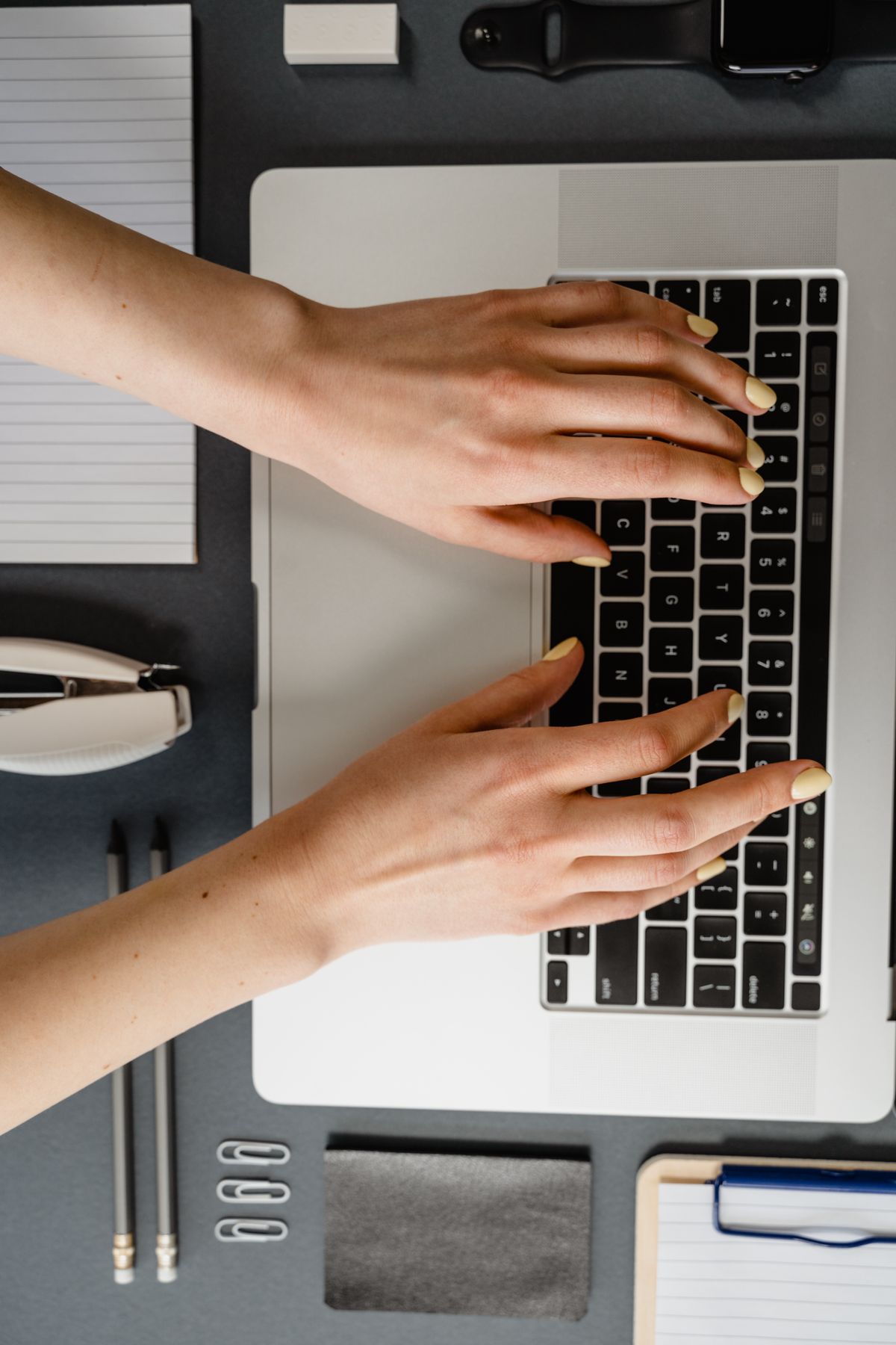 Overhead shot of a person with yellow nail polish typing on a laptop keyboard