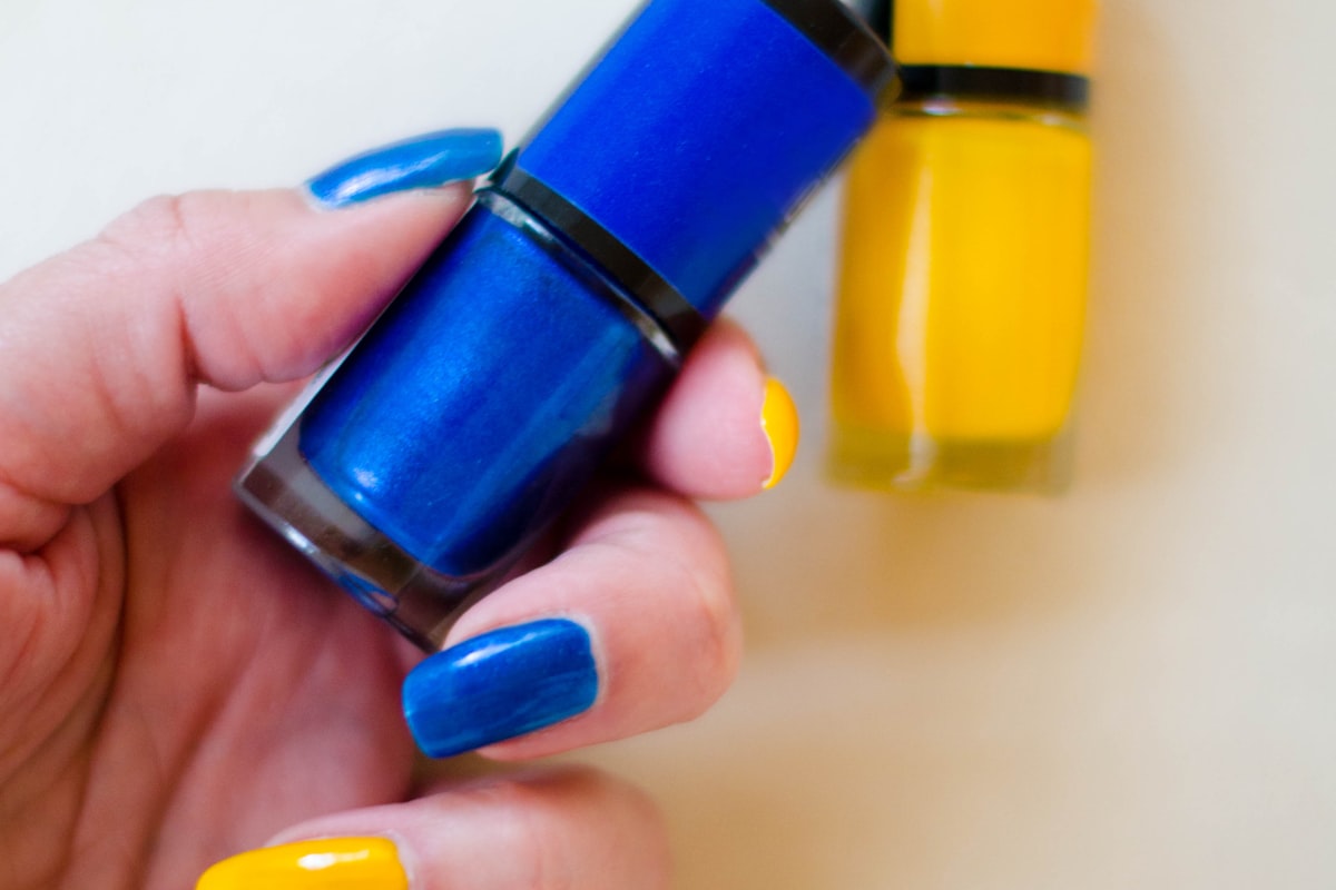 A hand holding a bottle of yellow nail polish against a neutral background