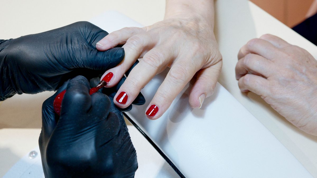 Nail technician applying deep red polish to a client at a salon