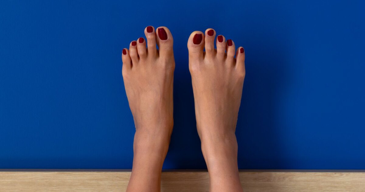 Overhead view of feet with deep oxblood red toe nail colors against a blue wall