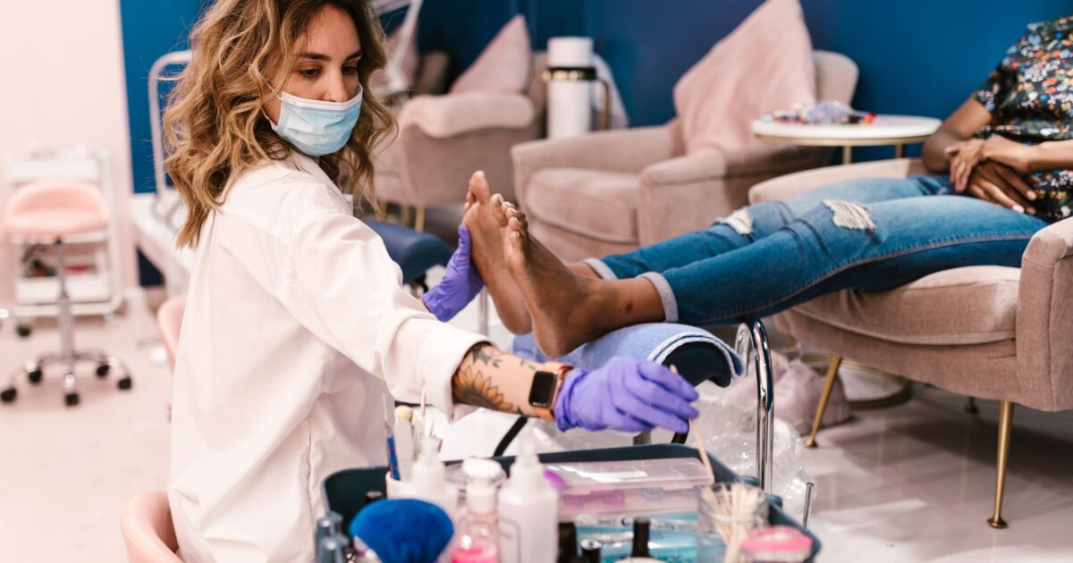Nail technician in gloves giving a client a pedicure in a modern salon