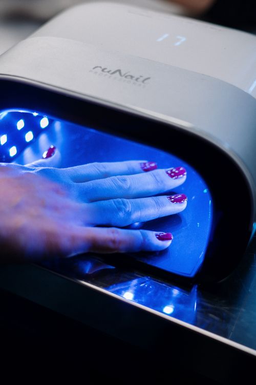 Hand with nail polish curing under a UV lamp during a professional gel nail manicure