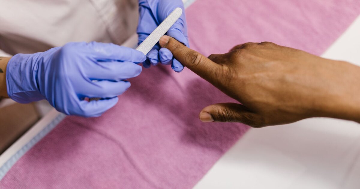 Nail technician filing a client nail to shape during a salon consultation