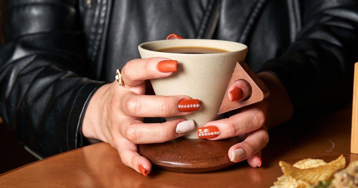 Terracotta orange nails holding a coffee cup under warm indoor light