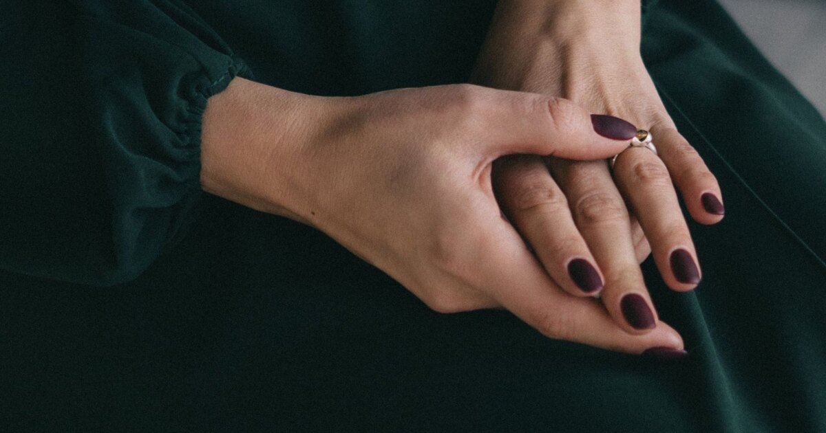 Deep plum matte nails resting on a dark green dress
