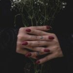Deep burgundy mulled wine nails on clasped hands against a dark background
