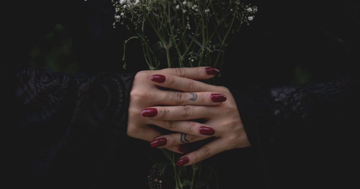 Deep burgundy mulled wine nails on clasped hands against a dark background