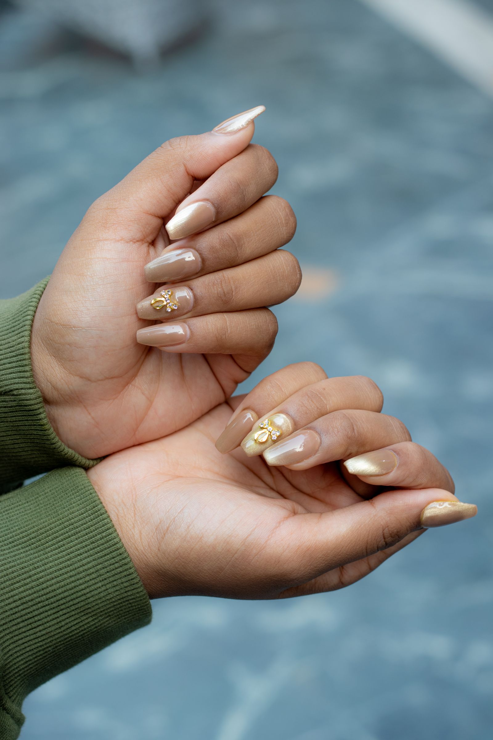 October nails in gold chrome with 3D gold charm accents on a deeper skin tone