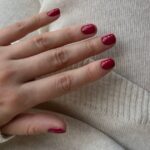 October nails 2026 in deep cherry red on short square nails, resting on a cream knit sweater