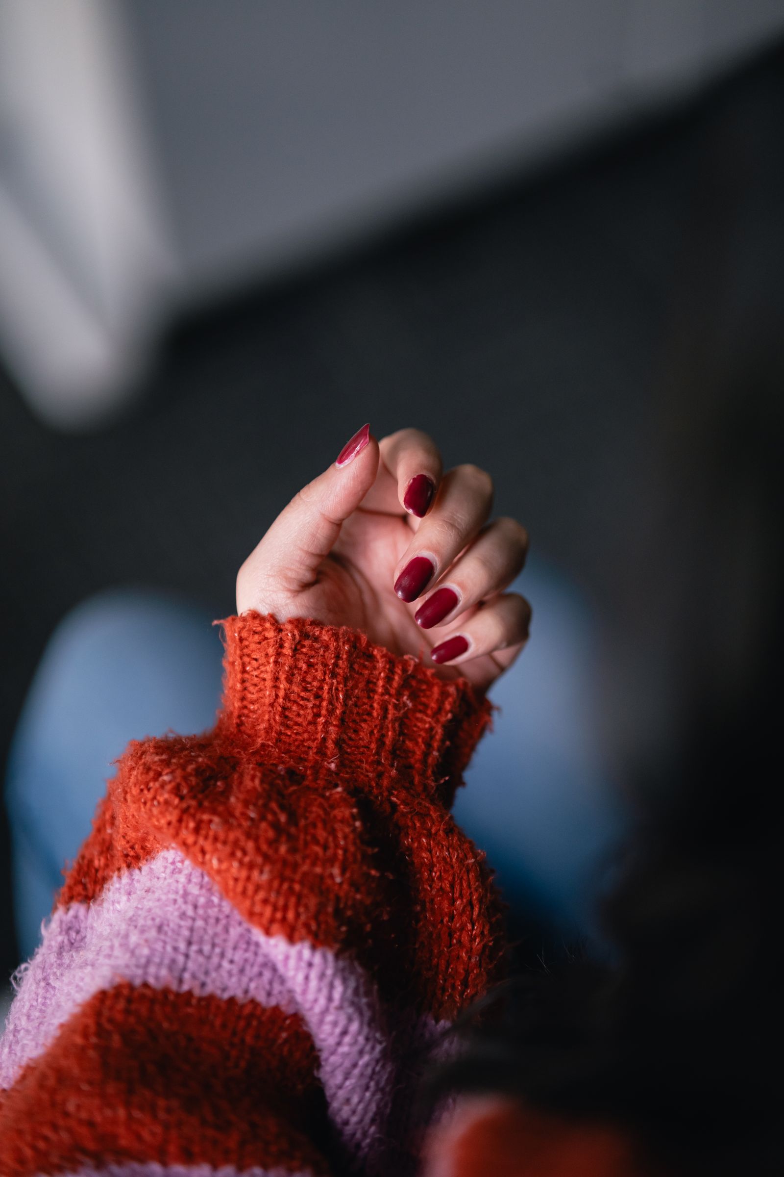 Short burgundy October nails against a rust and pink striped autumn sweater