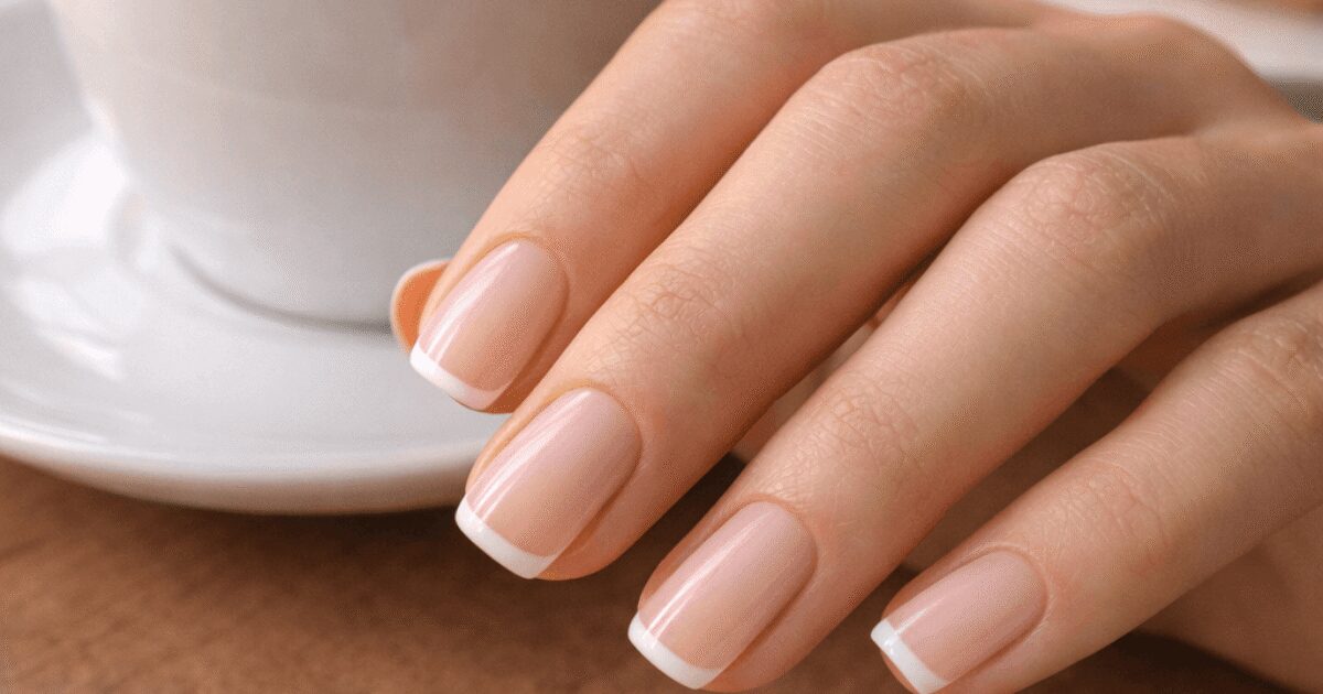 Short French tip acrylic nails resting beside a latte and croissant on a wooden cafe table