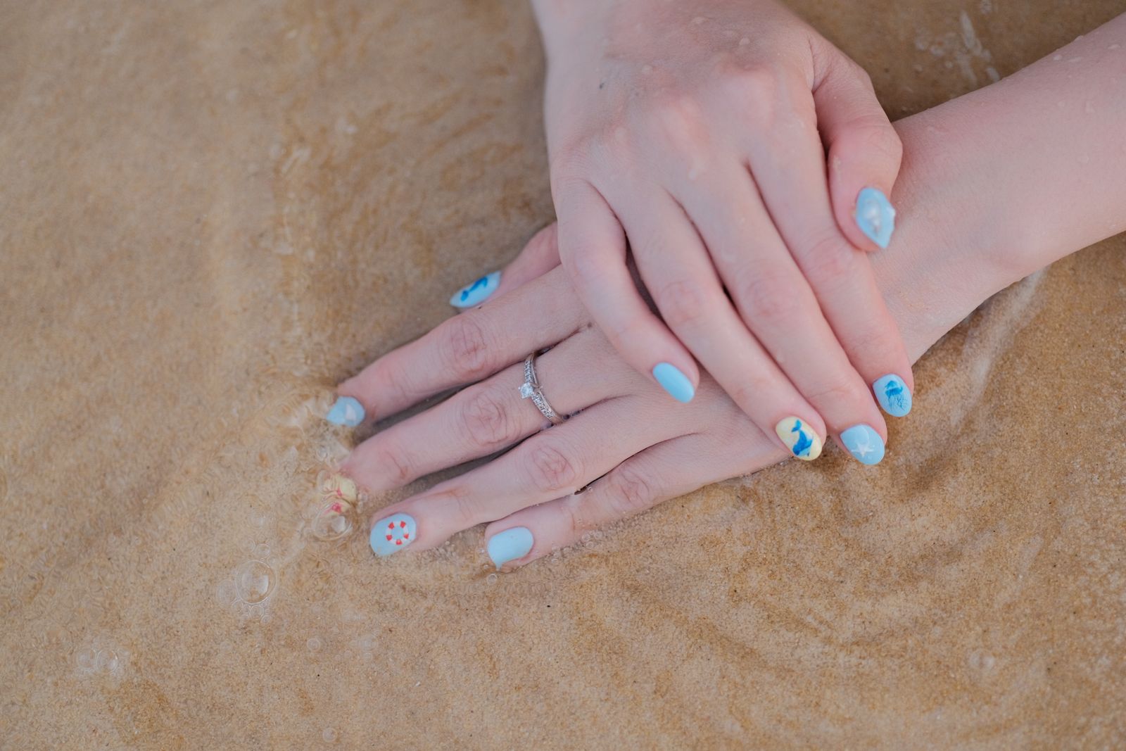 Beach-themed surfside nail art photographed against sand and shoreline waves