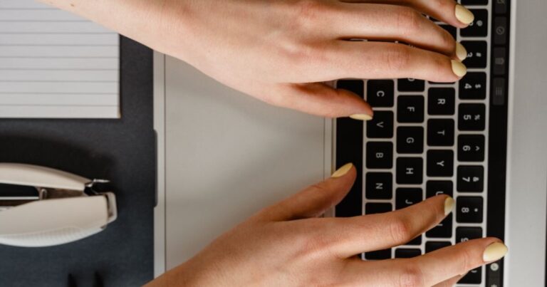 Hands with butter yellow gel polish typing on a laptop at a desk