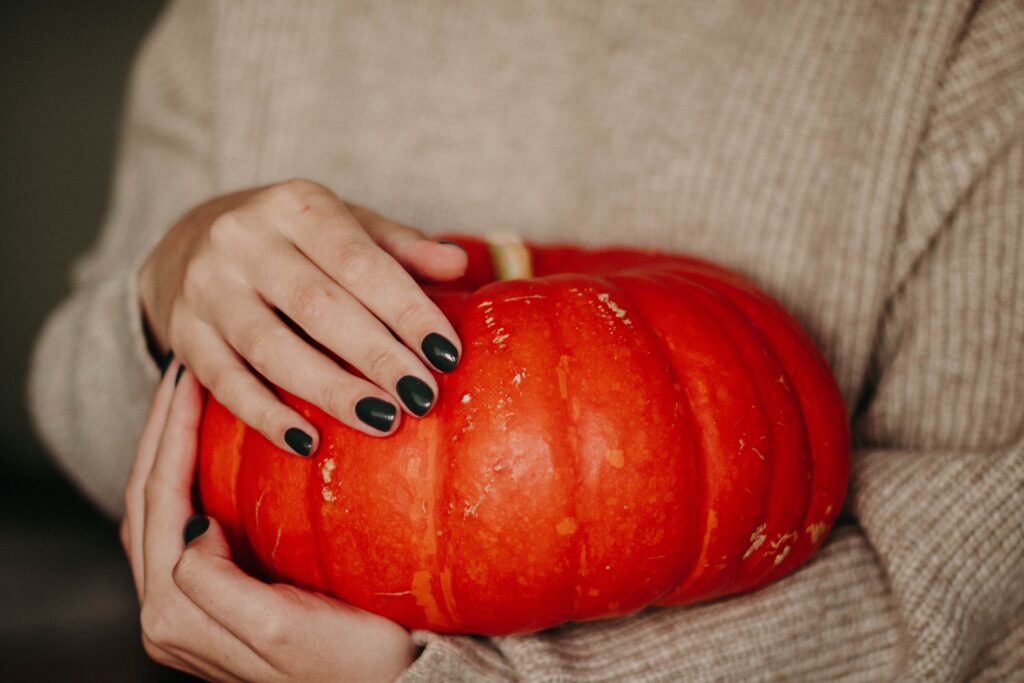 Short dark nails resting on an orange pumpkin, the classic Halloween pairing