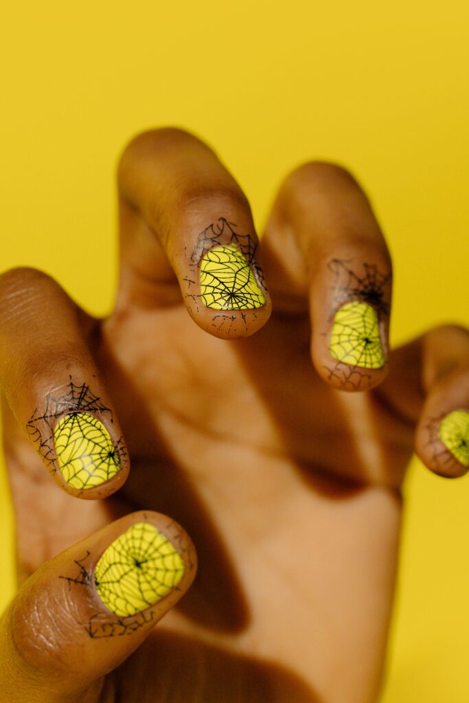 Short natural nails with black spider web nail art on neon yellow polish
