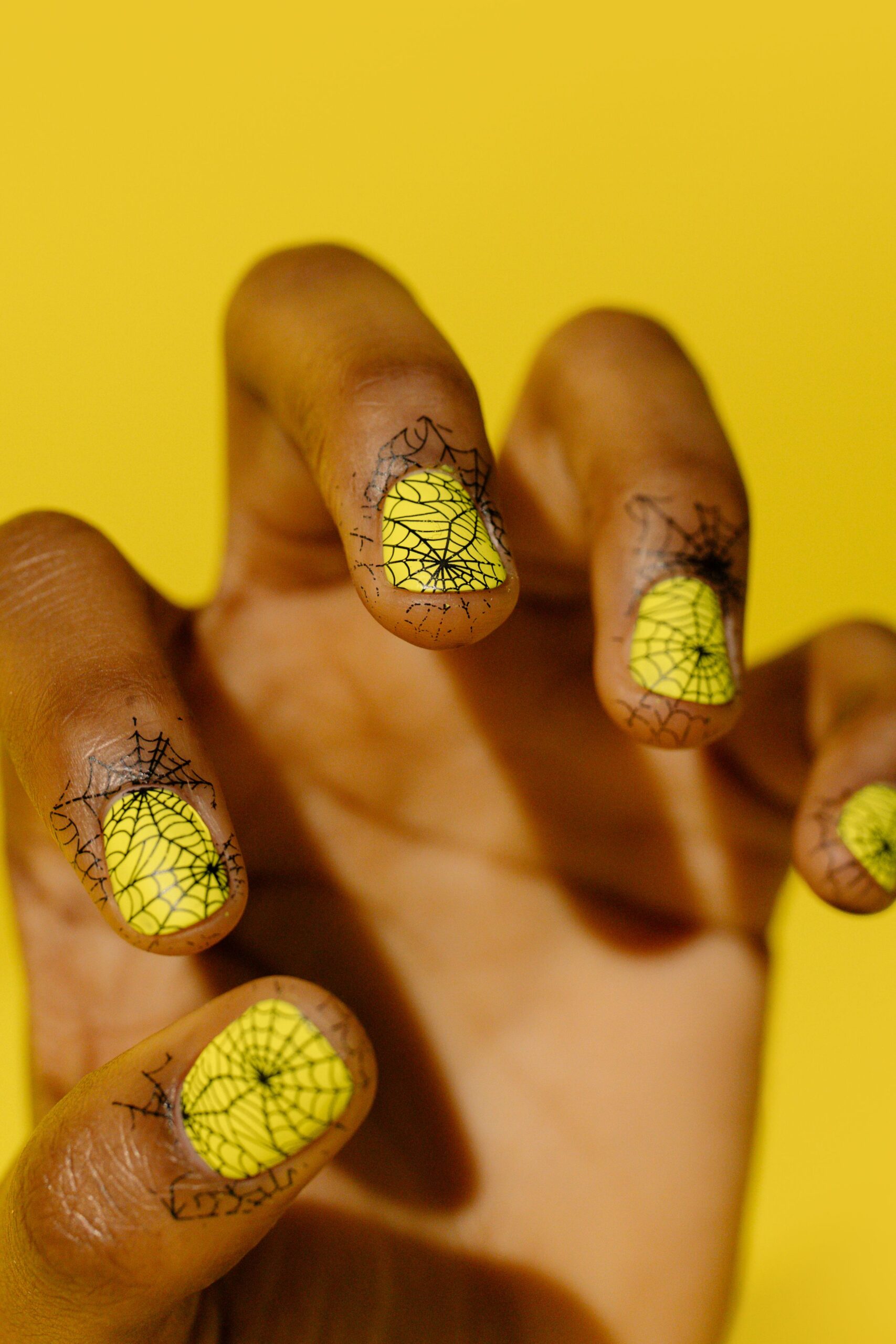Short natural nails with black spider web nail art on neon yellow polish